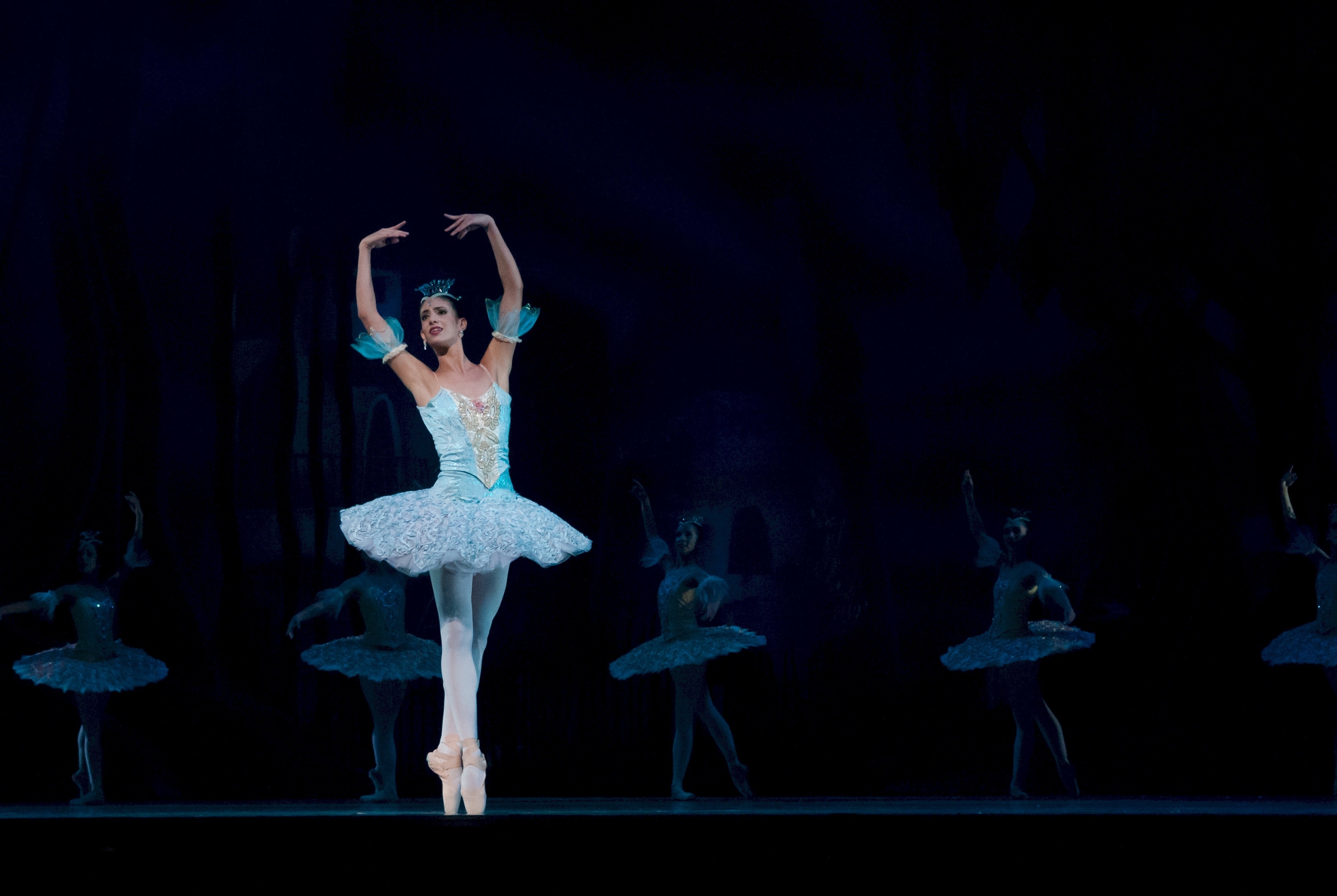 Ballerina in a white tutu dancing en pointe on a dark stage, with other dancers behind her