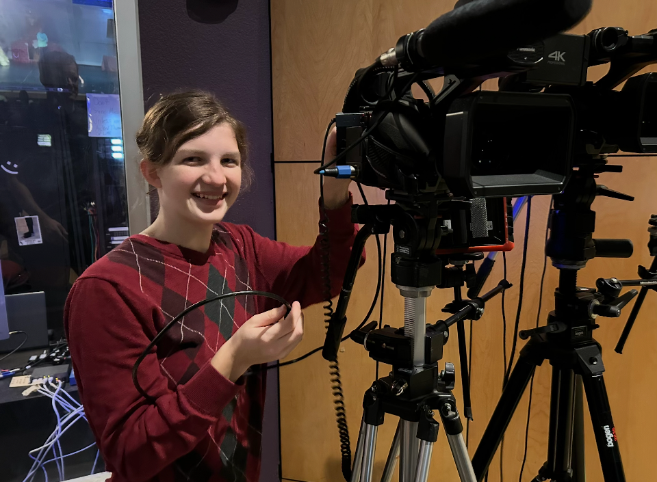 Lyla smiling while operating a professional video camera on a tripod