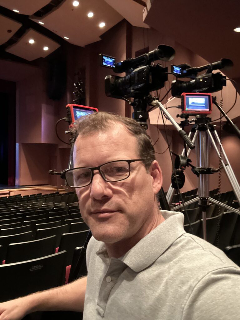 Ryan Andrews seated in a theater beside a multi-camera recording setup